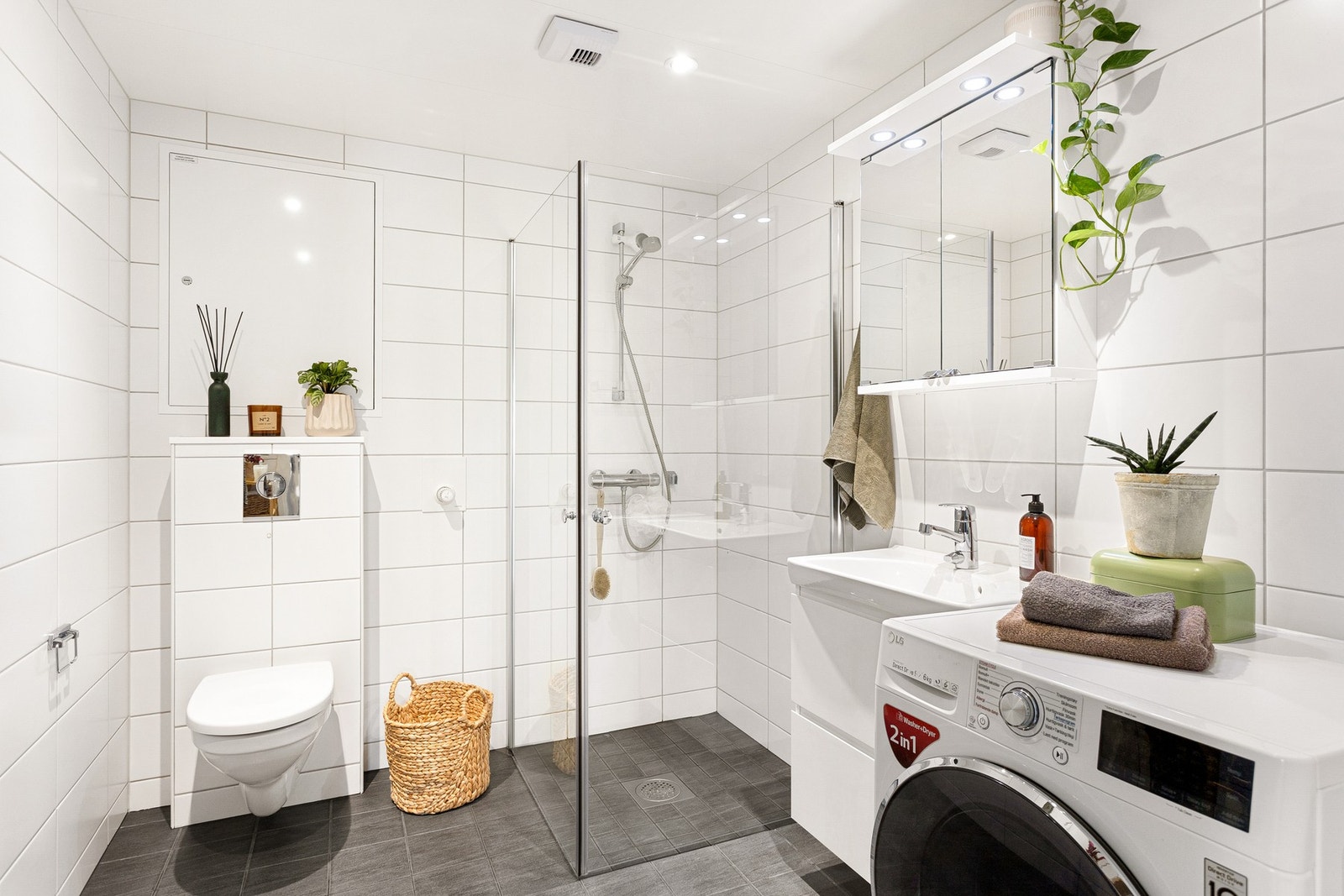 Badet er moderne og tidløst innredet med lysegrå fliser på gulv, hvite fliser på vegg og spotter i taket Galleribilde