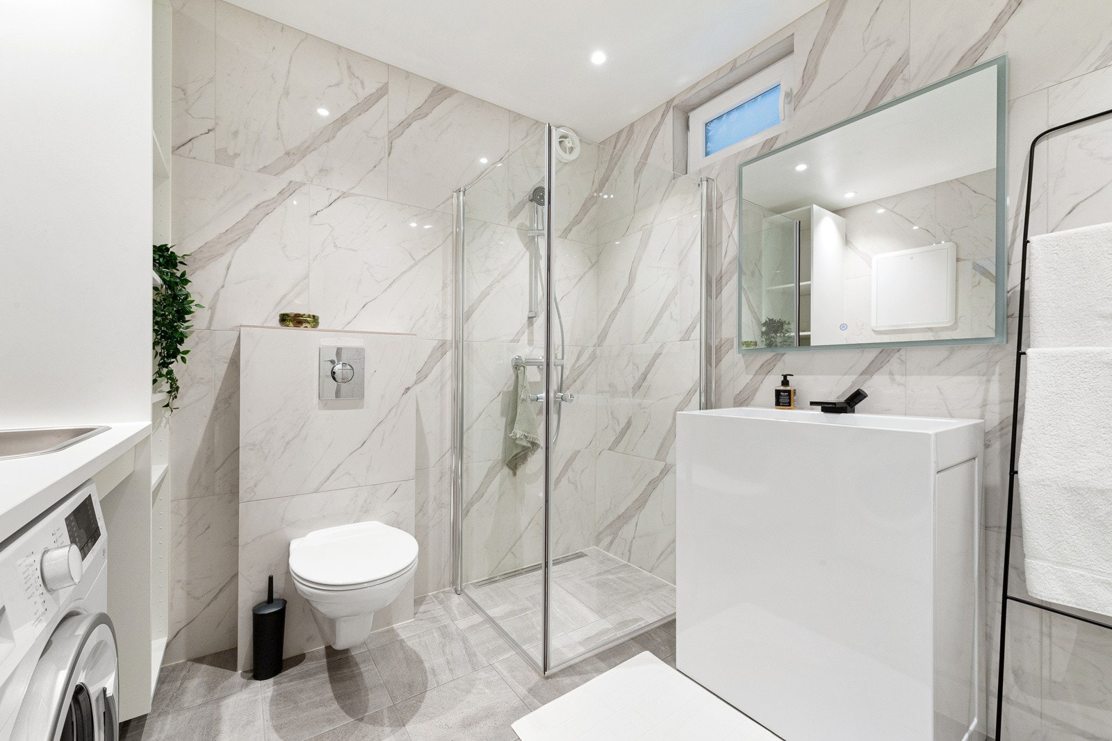 Badet inneholder møblement, servant, speil, veggehengt toalett, dusjhjørne, benkeplate m.m. Det er varmekabler i gulvet. Galleribilde