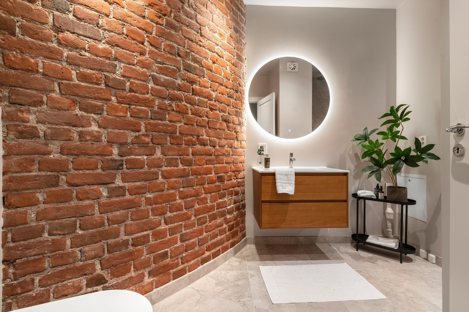 Badet er innredet med speil med backlights, nedfelt servant med tilhørende skuffer, dusjhjørne og et vegghengt klosett Galleribilde