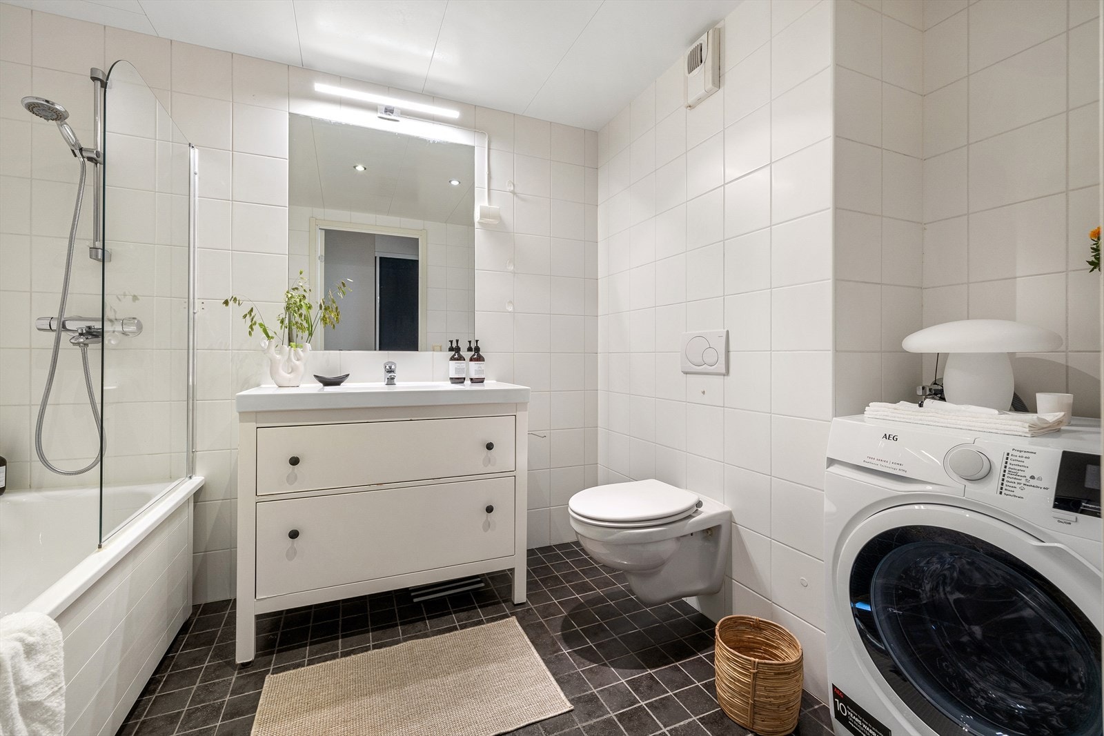 Badet er innredet med vegghengt toalett, baderomsinnredning og badekar med glassdør og dusjarmatur Galleribilde