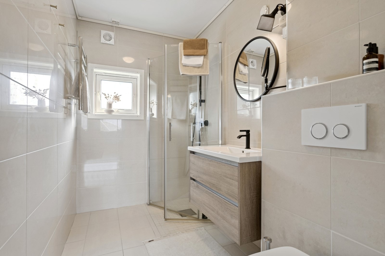 Badet er utstyrt med innfellbare dusjdører, mekanisk avtrekk, rørfordelingsskap, servant, servantskap og veggmontert wc. Galleribilde