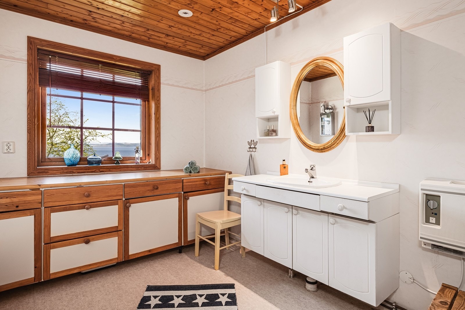 Badet i 1. etasje har gulvbelegg med varmekabler og vinyltapet på veggene. Badet er innredet med baderomsinnredning med underskap, benkeplate og nedfelt servant i tillegg til en romslig innredning under vinduet. Galleribilde