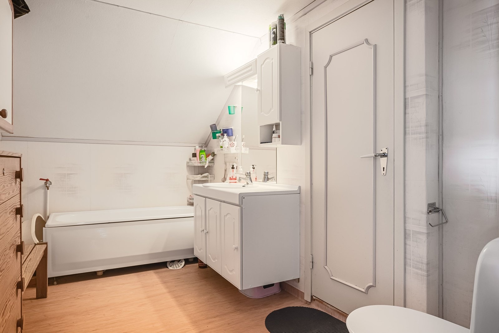 Bad i 2. etasje med adkomst fra den ene stua. Badet har belegg på gulvet og vinyltapet på veggene. Det er utstyrt med gulvmontert toalett, badekar og baderomsinnredning med servant. Galleribilde