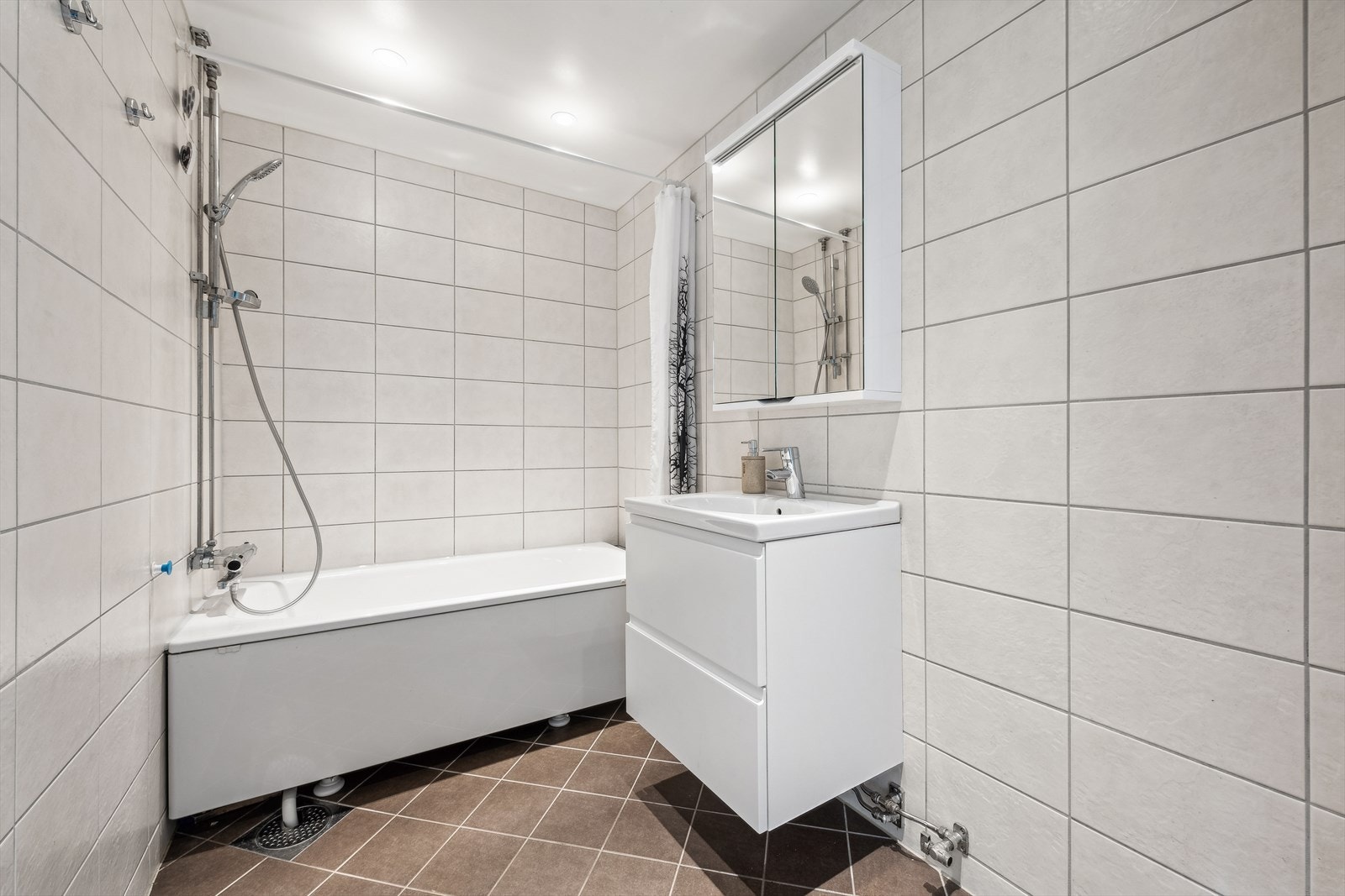 Flislagt bad med varmekabler i gulv, utstyrt med innredning, servant, speilskap, samt badekar med dusj. Galleribilde