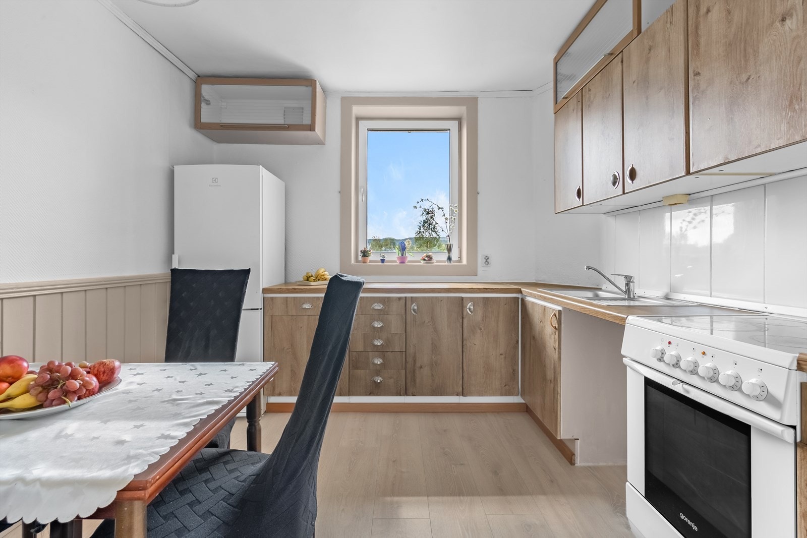 Kjøkkeninnredning med glatte fronter. Fliser på vegg over benkeskap. Laminat benkeplate med nedfelt kum i rustfritt stål. kjøleskap og stekeovn følger med salget. Galleribilde