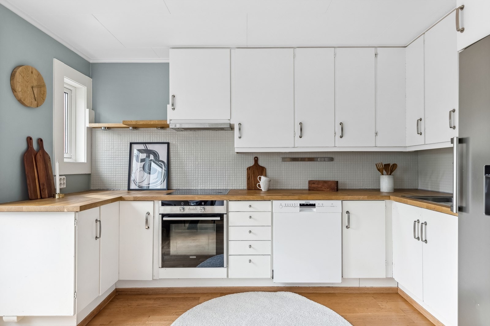 Kjøkkenet har hvite glatte fronter, benkeplate, rustfri servant, ventilator, integrert komfyr og platetopp. Galleribilde