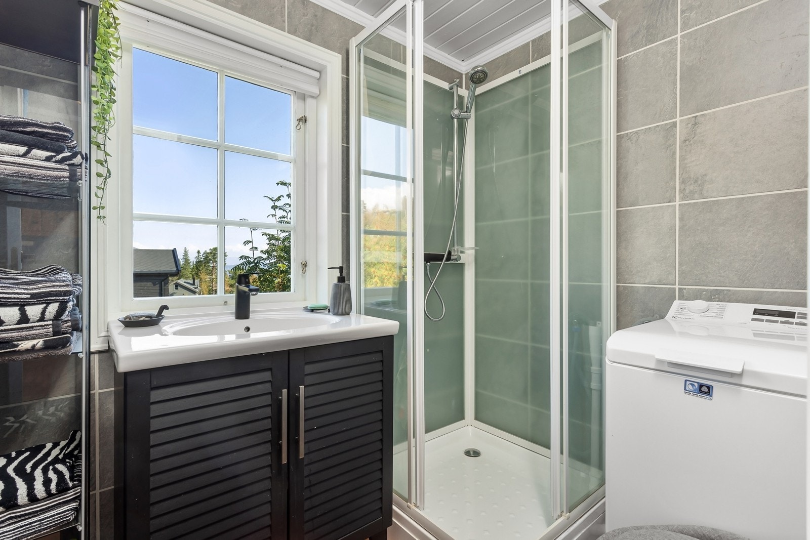 Badet har innredning med heldekkende servant, toalett, dusjkabinett og opplegg for vaskemaskin. Rommet ble oppgradert med ny innredning og veggplater i 2021. Galleribilde