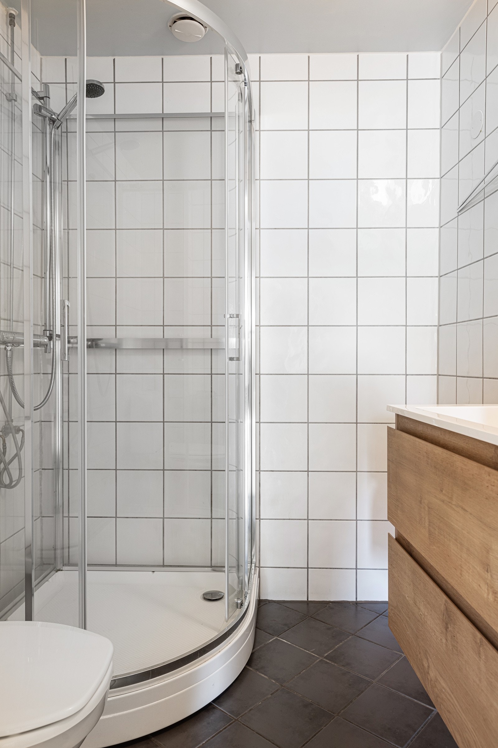 Bad med toalett, nyinstallert dusjkabinett i herdet glass, veggspeil med overliggende belysning, baderomsinnredning med finerte fronter og heldekkende servant. Galleribilde