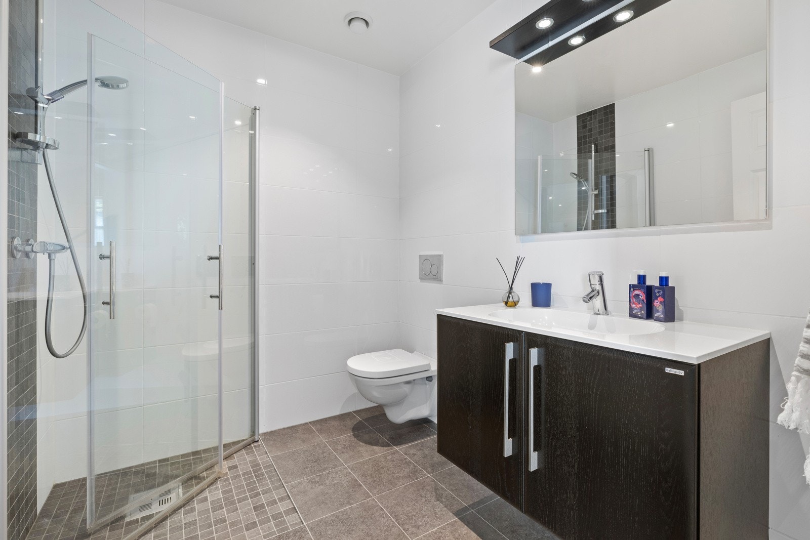 Bad i 1. etasje - dusjhjørne, vegghengt toalett, innredning med heldekkende servant og speil med overlys Galleribilde