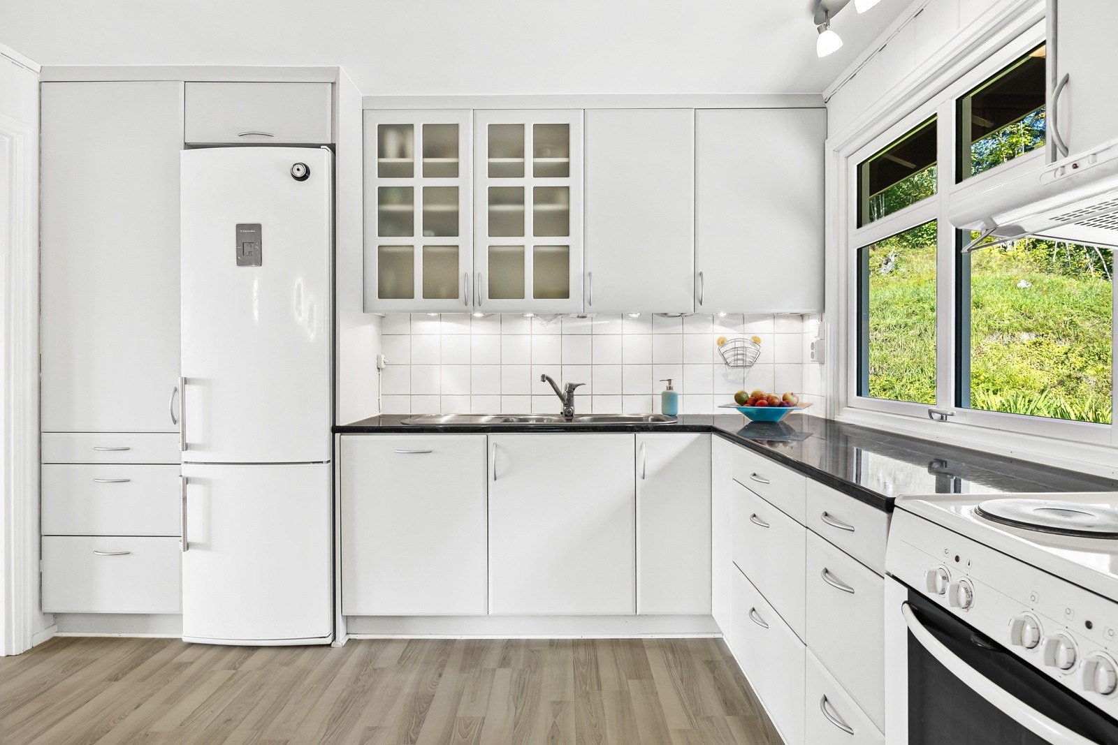 Kjøkkenet har lys grå innredning med slette fronter, laminat benkeplate og fliser mellom benk og overkskap. Galleribilde