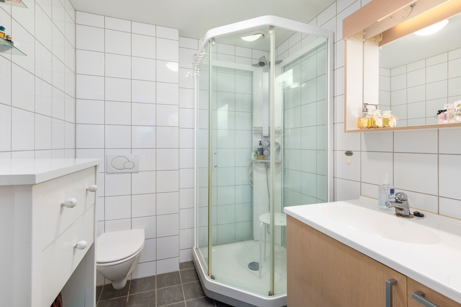 Badet er flislagt og har dusjkabinett, servant og vegghengt toalett. Galleribilde