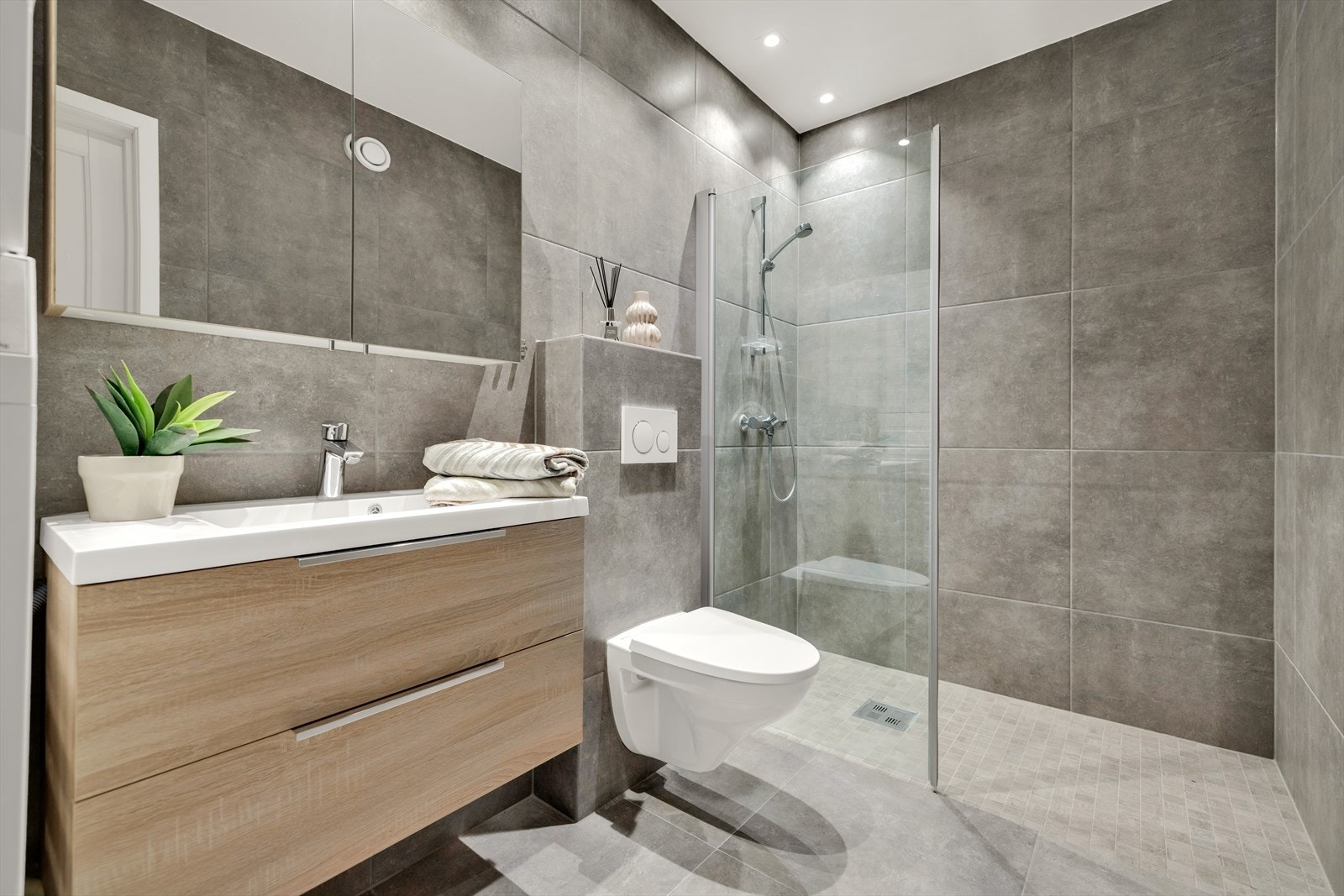 Pent baderom med servant med innredning og speil. Vegghengt toalett og dusj. Galleribilde