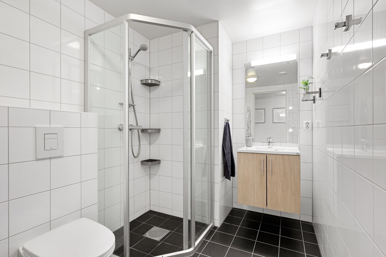 Badet er et avlangt rom i klassisk stil, med hvite fliser på veggene og sorte fliser over gulvvarme. Galleribilde