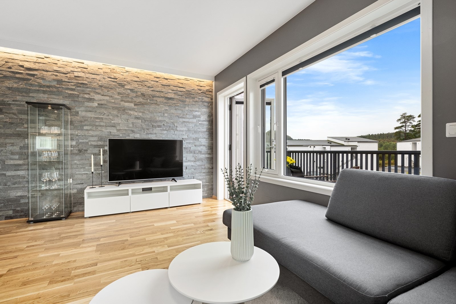 Det naturlige samlingspunktet i leiligheten er et tiltalende allrom med stue og kjøkken i ett, men likevel med klare soner. Allrommet har parkettgulv og slette, gråmalte vegger kombinert med en fondvegg kledd med naturstein. Galleribilde