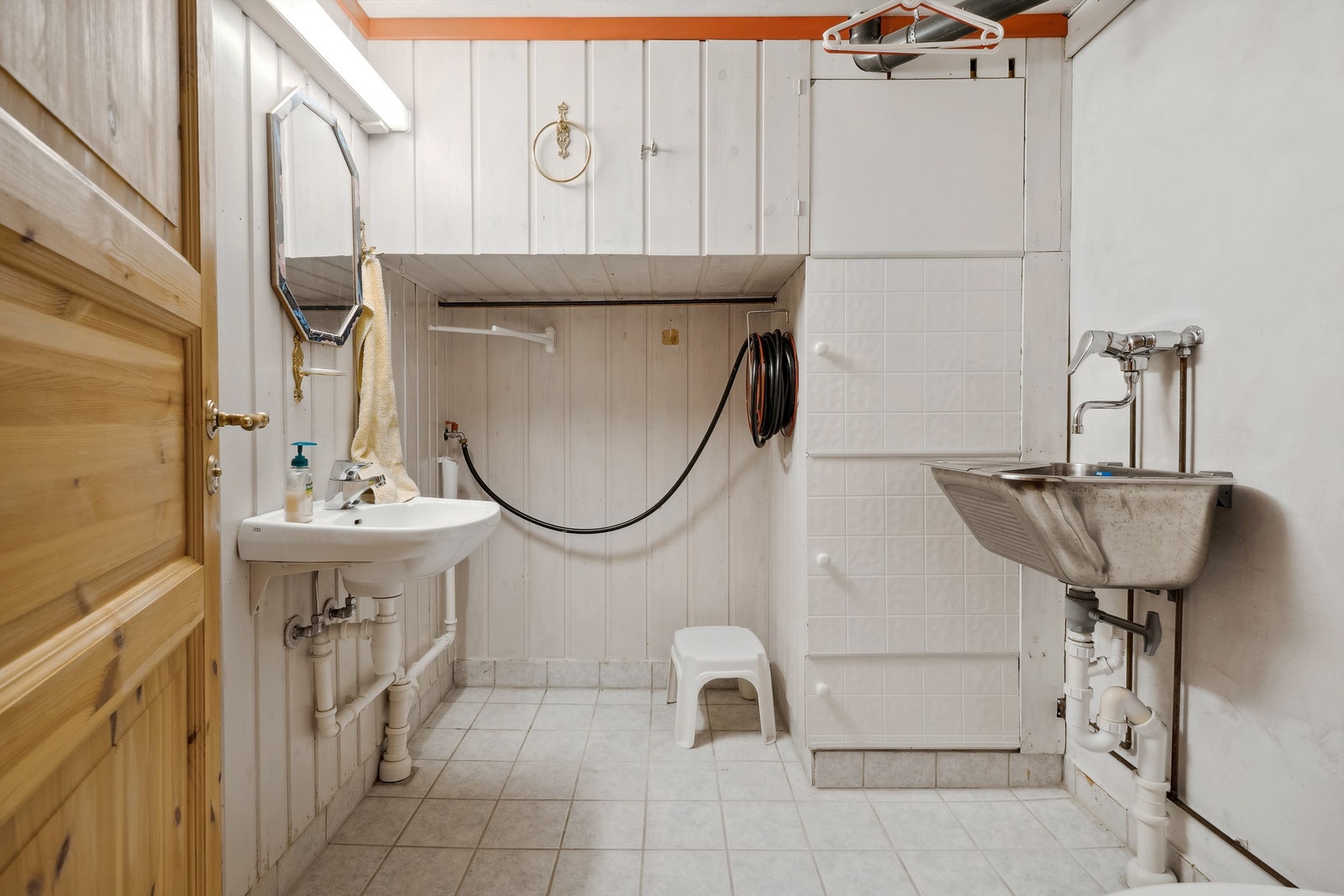 Eldre bad med flislagt gulv med varmekabler. Vegger og tak med malt panel. Innredet med enkel servant, skyllekar og dusjgarnityr på vegg med dusjforheng. Galleribilde