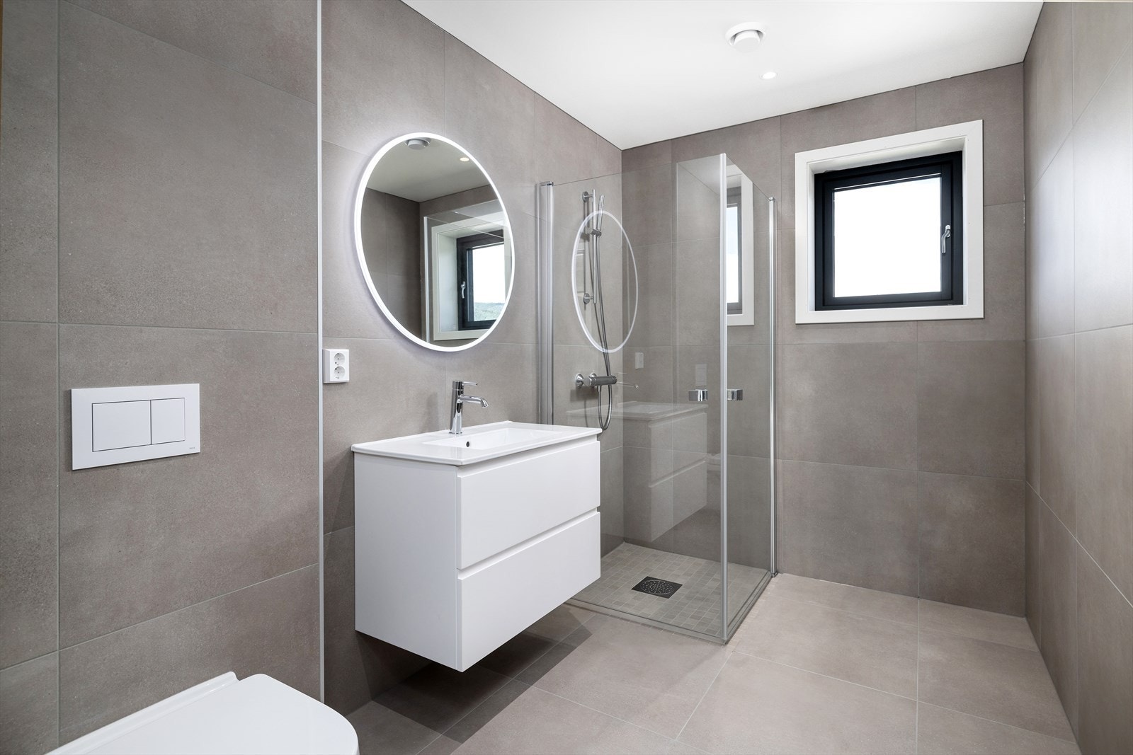 Flislagt bad med vegghengt toalett, dusjvegger og baderomsinnredning med servant Galleribilde