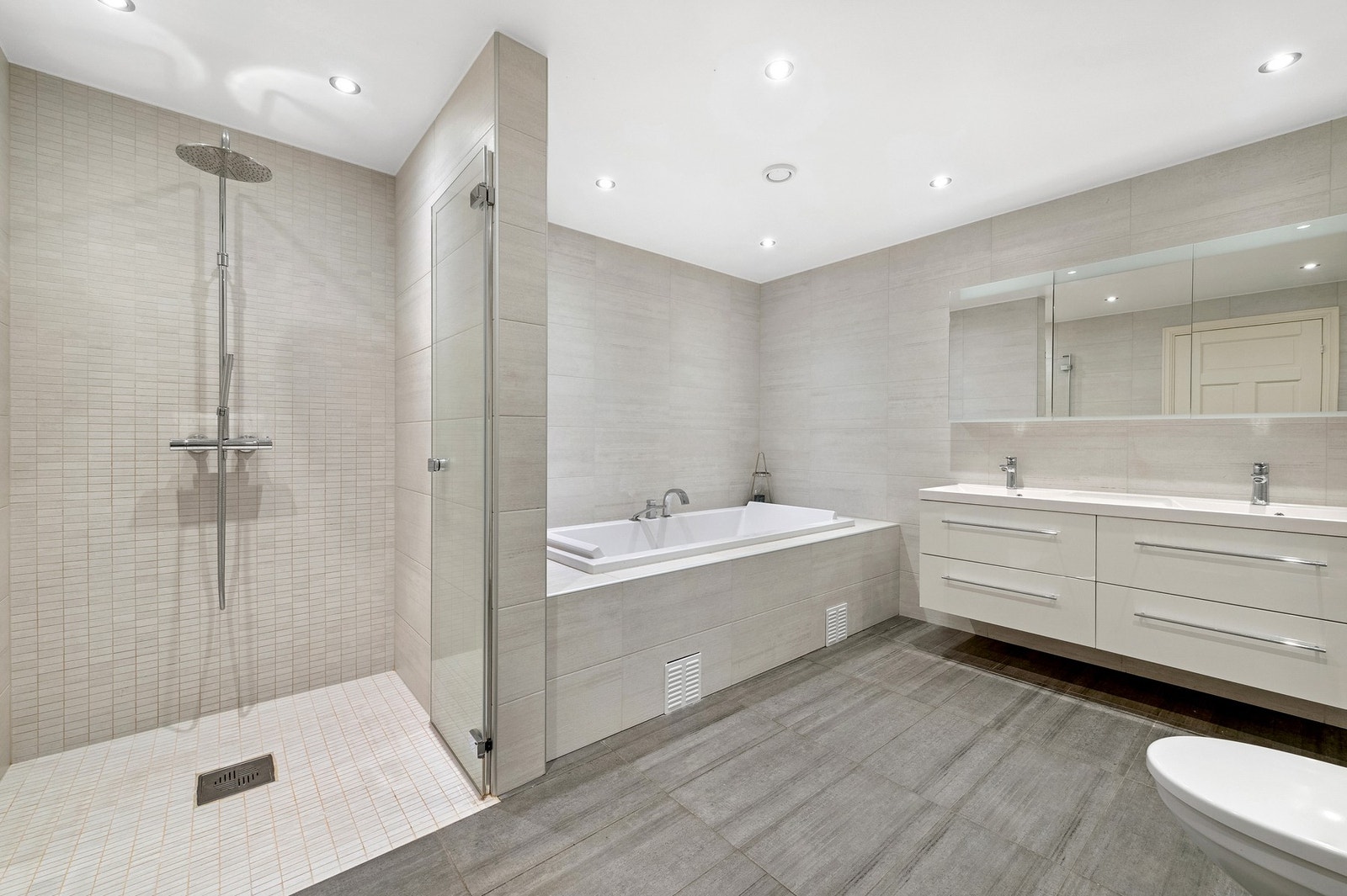 Moderne bad fra 2014 med flislagt gulv, downlights, integrert badekar, regndusj og dobbelvask Galleribilde