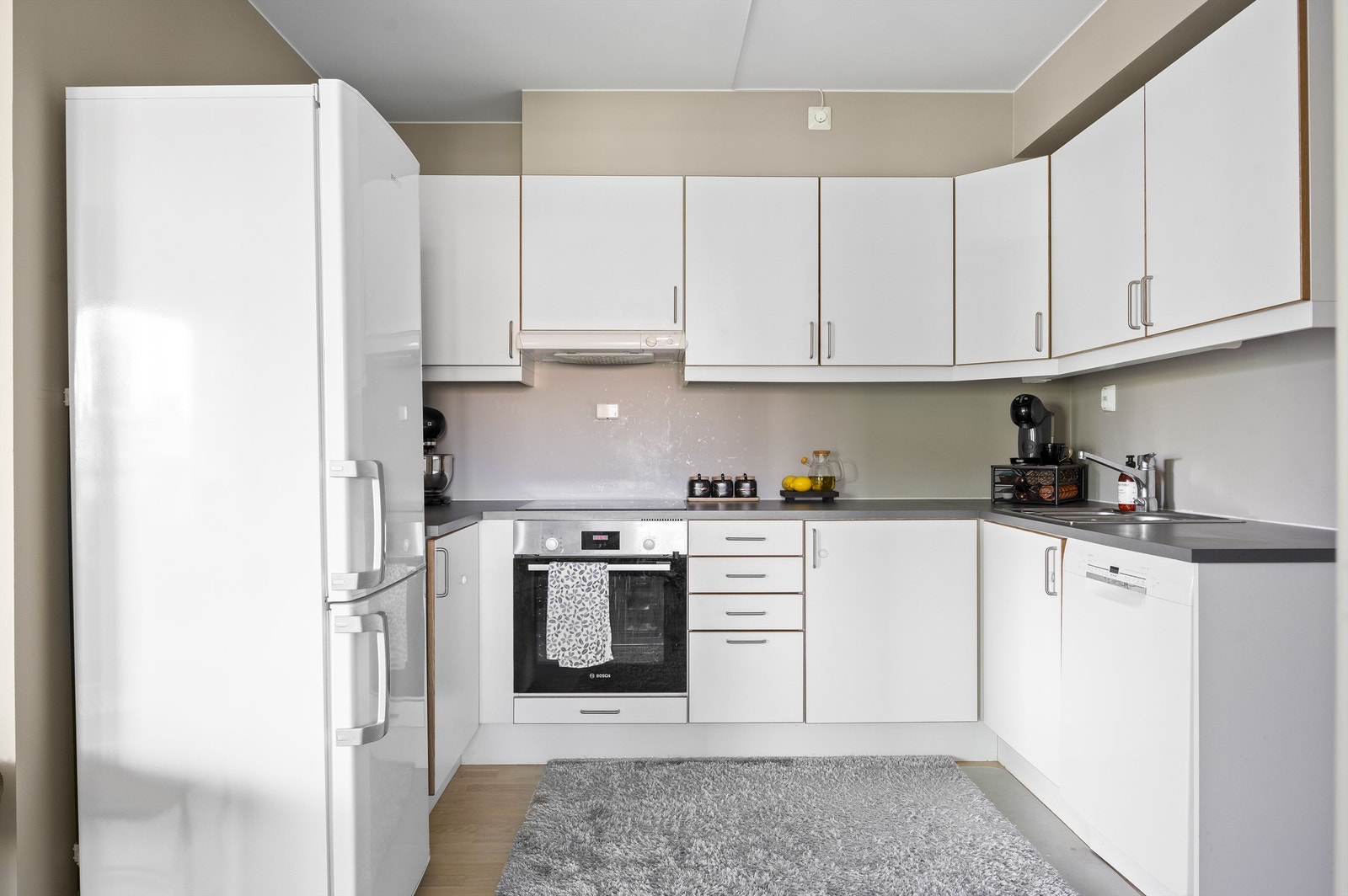 Innredning med hvite glatte skapfronter, laminat benkeplater, nedfelt rustfri oppvaskkum og ett-greps armatur Galleribilde