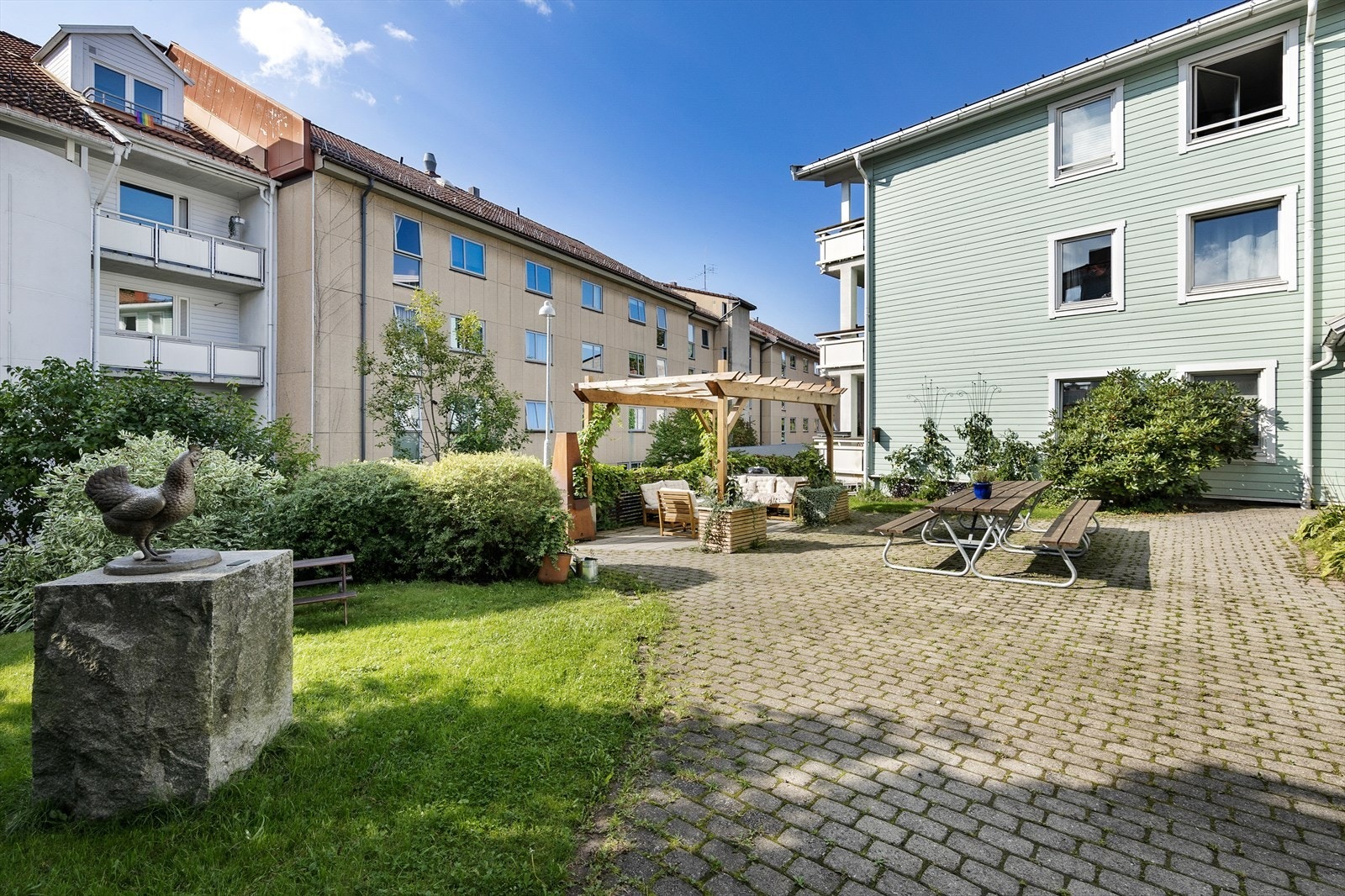 Bakgården er pent opparbeidet med steinlagte partier, gressplen, frodig beplantning og sittegrupper med utepeis. Galleribilde