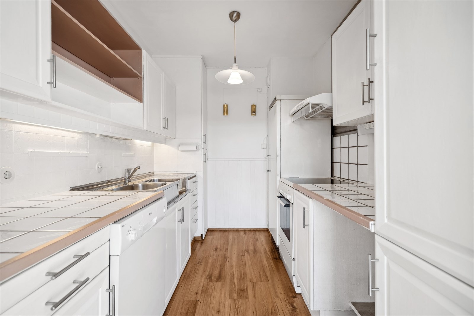 Kjøkkenet har et klassisk og rent utrykk med malte, hvite profilerte fronter, flislagt benkeplate med komplementerende fliser over. Den gode romfølelsen tilrettelegger for optimal kokkelering med generøs benk/skapplass. Galleribilde