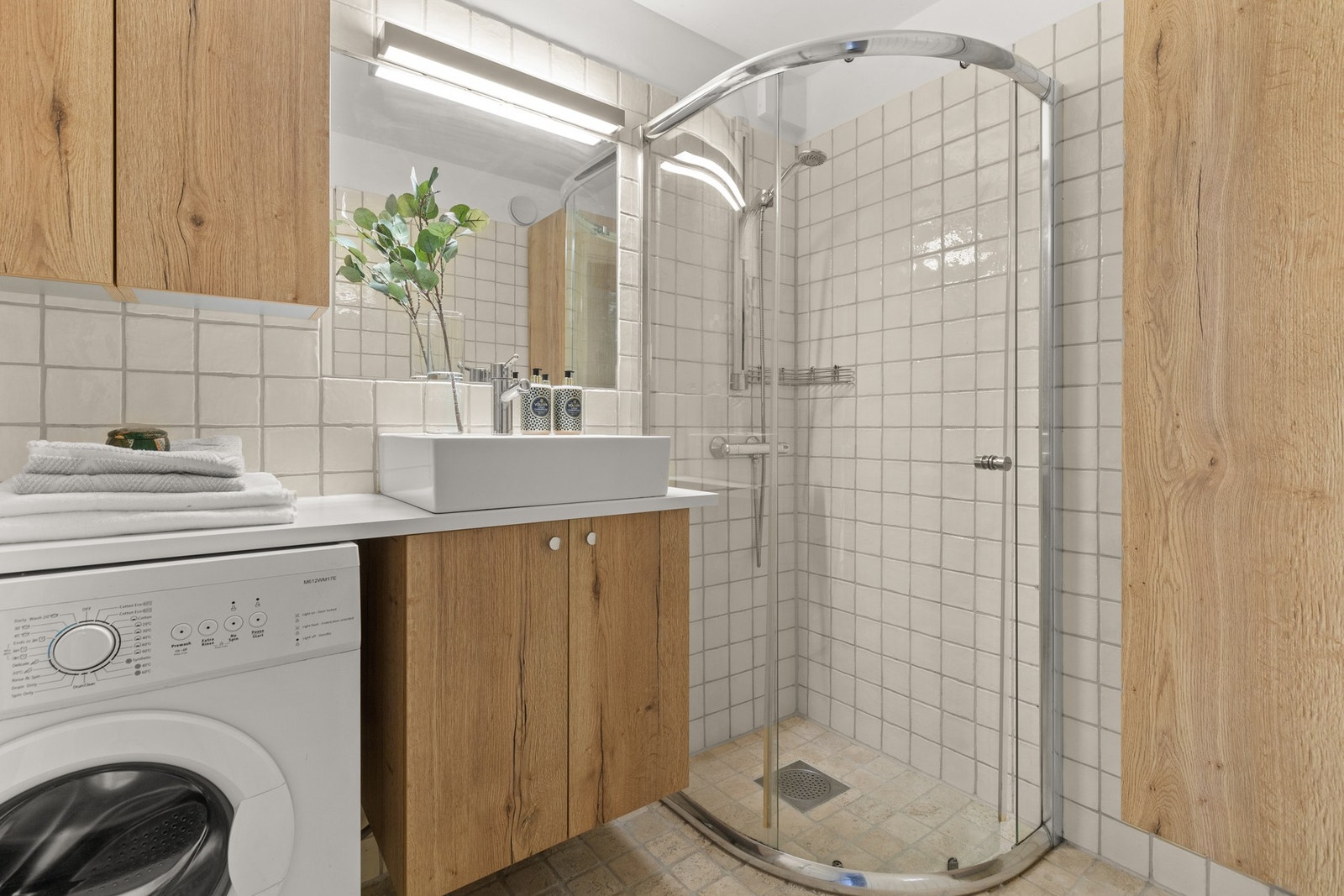Badet har dusj på gulv med dører i herdet glass.
Servant og opplegg for vaskemaskin. Galleribilde