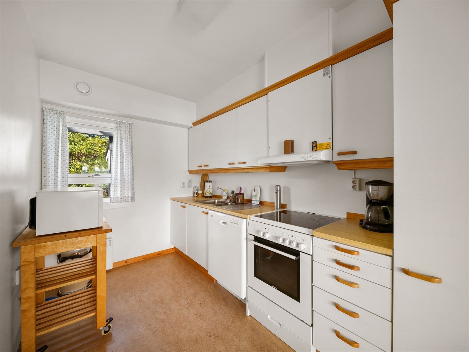 Kjøkkenet inneholder en eldre innredning med glatte finerfronter og laminert benkeplate. Galleribilde