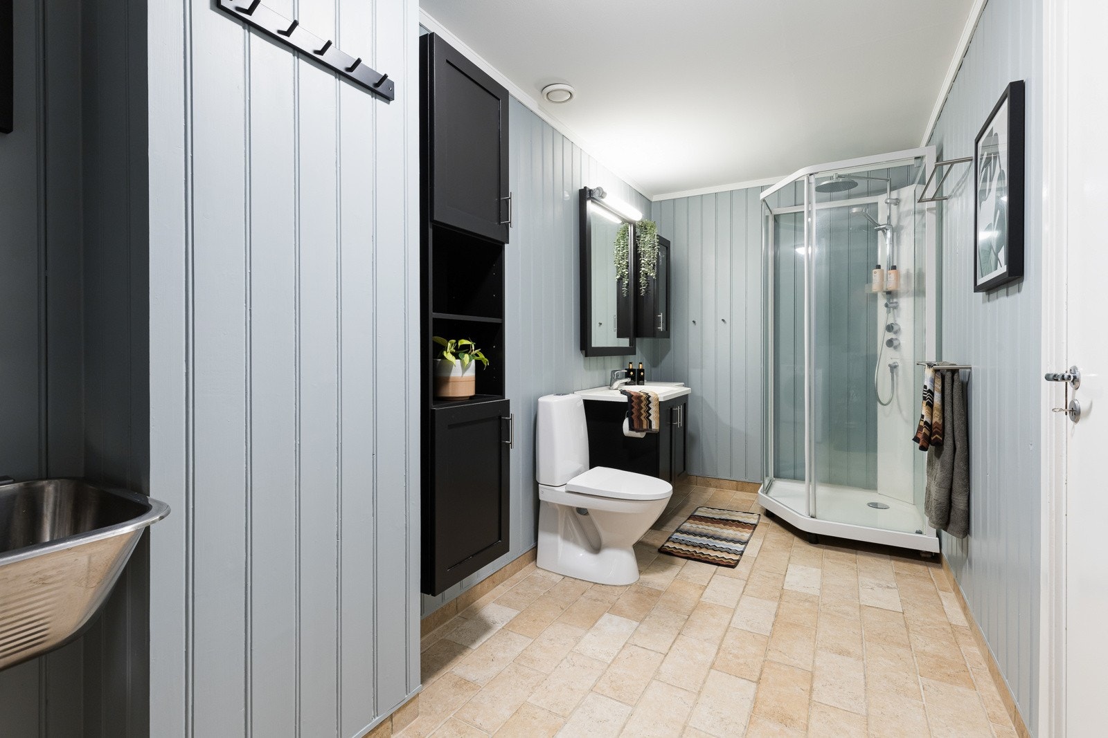 Badet fremstår som romslig og velholdt, med lyseblå panel på veggene og sandfargede fliser på gulv med gulvvarme. Galleribilde