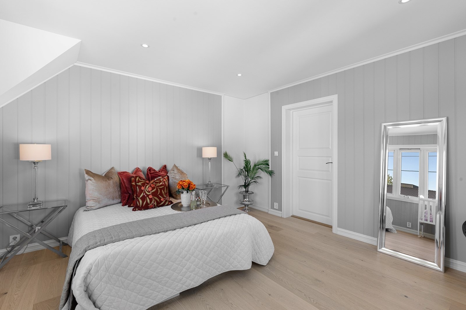 Pent innredet hovedsoverom med trepanel på vegg malt i den samme lys grå fargetonen og 1-stavs laminat på gulv. Galleribilde