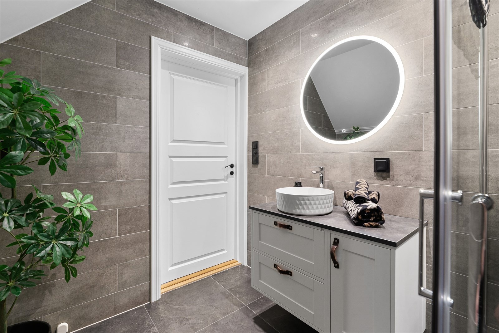 Baderomsinnredningen har et moderne men samtidig klassisk preg med fin bolleservant, rom for oppbevaring i underskuffer og skap og rundt speil med led lys. Legg merke til skinn detaljene på baderomsinnredningen. Galleribilde