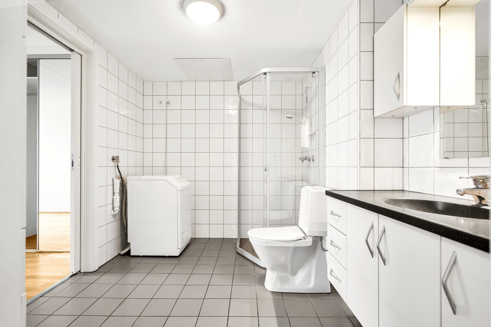 Badet har gulvvarme, dusjvegger i glass, toalett, servant med underskap og opplegg til vaskemaskin Galleribilde