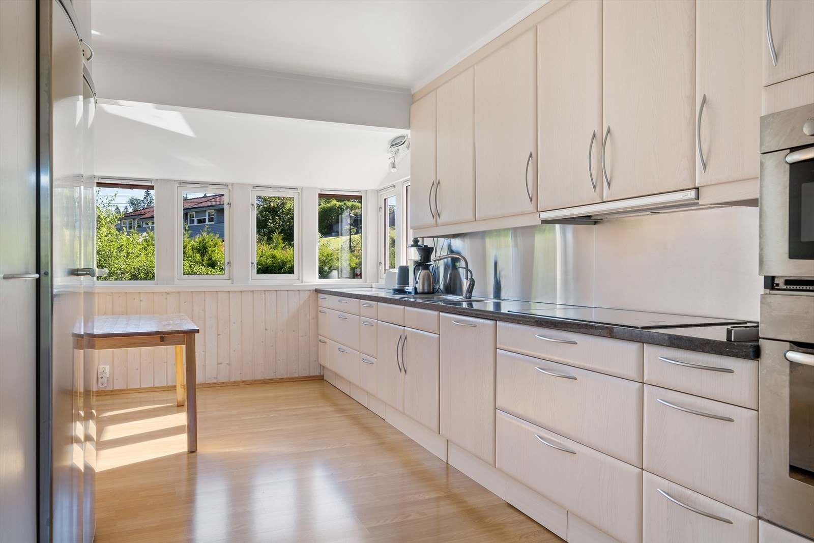 Kjøkkeninnredning fra 2005 med benkeplater av Larvikitt, plateslått backsplash av rustfritt børstet stål og slette skapfronter. Galleribilde