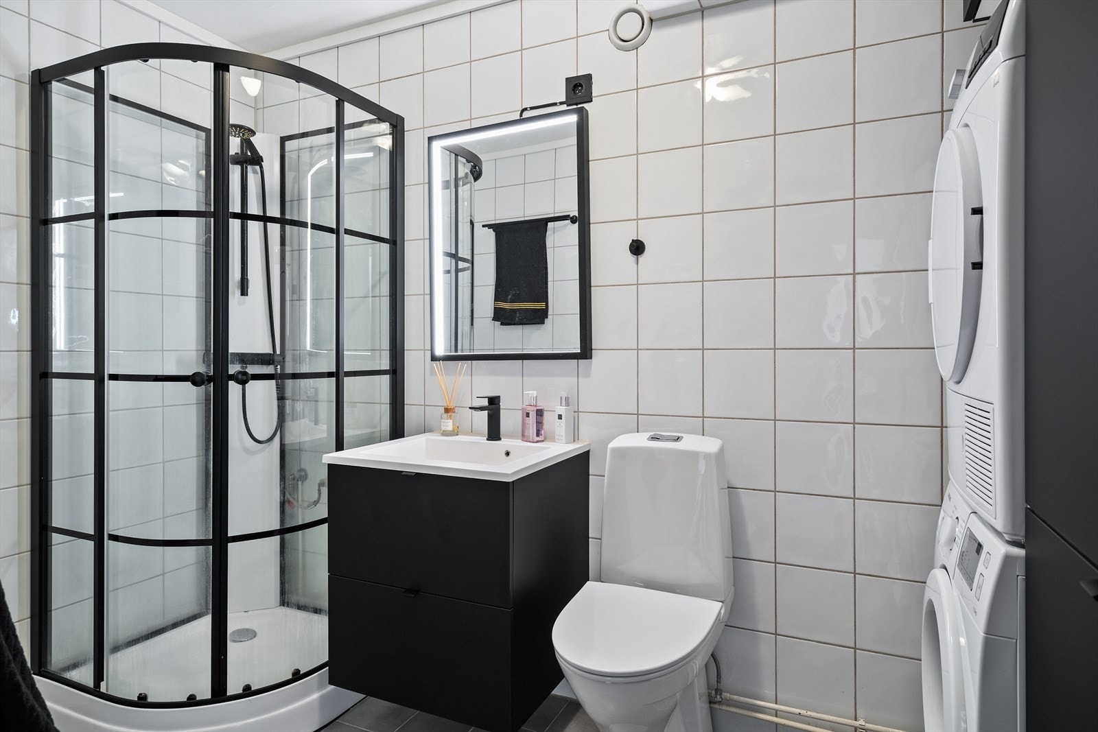 Leiligheten har et flislagt bad med dusjkabinett, servant, speil med lys, toalett og opplegg for vaskemaskin. Galleribilde