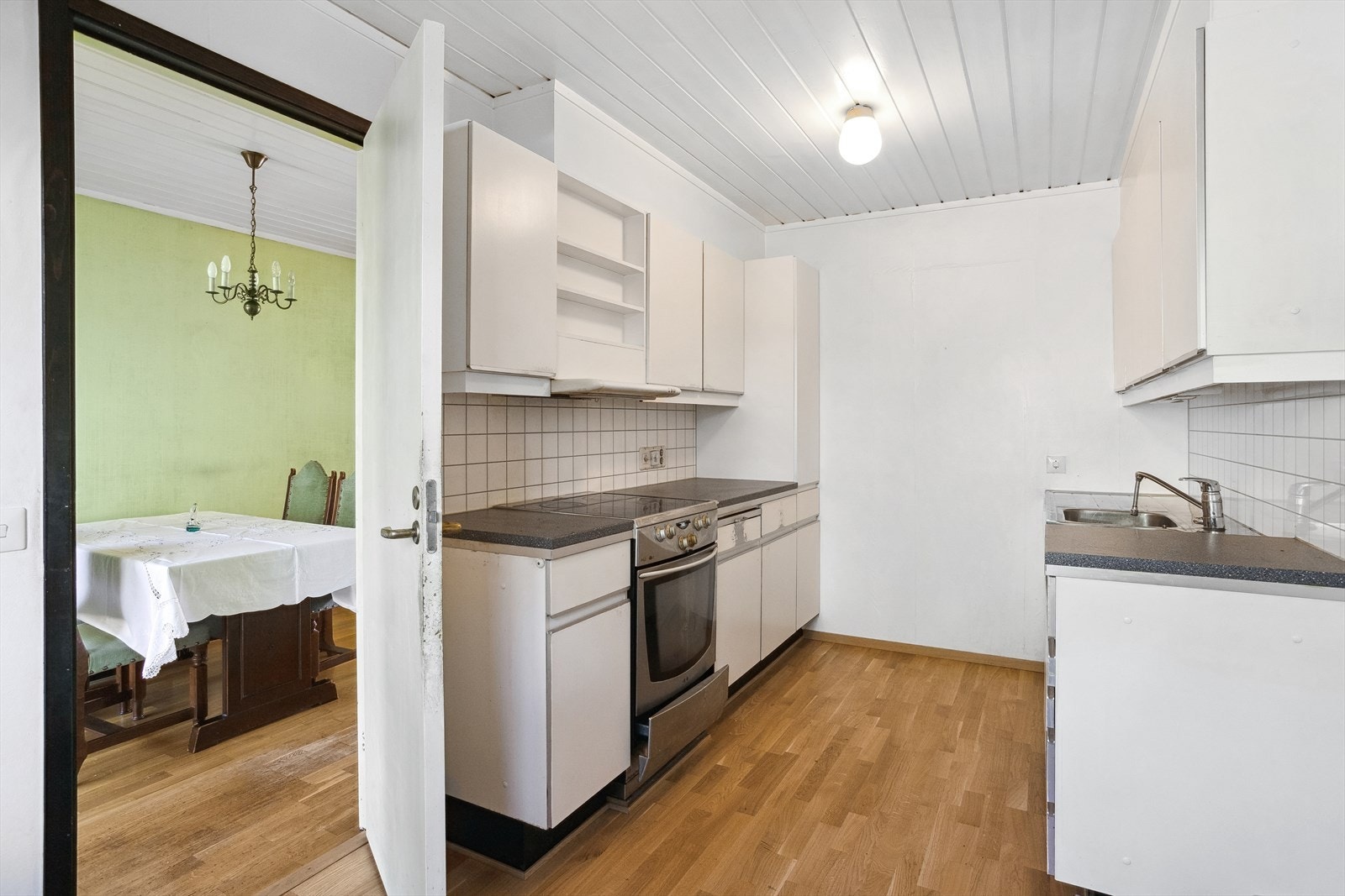 Eldre kjøkkeninnredning med malte glatte fronter, laminat benkeplate og rustfri benkebeslag med oppvaskkum. Galleribilde