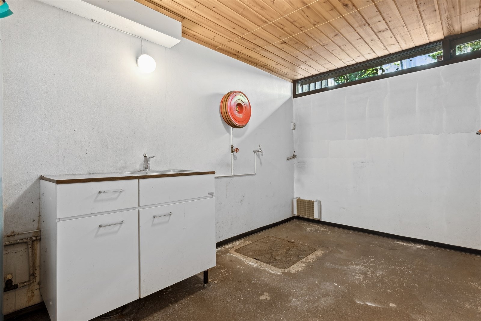 Eldre vaskerom bestående av betonggulv og malte murvegger. Innredning med lyse glatte fronter, benkeplate i laminat, rustfri oppvaskkum og plass for vaskemaskin. Galleribilde