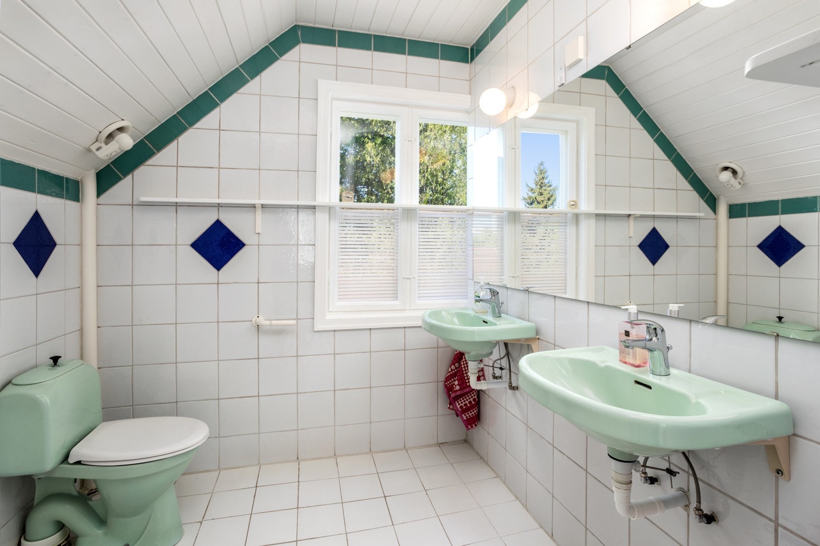 Badet har flislagte vegger og malt panel i himlingen. Utstyrt med klosett, badekar, dusjopplegg på veggen og to servanter Galleribilde