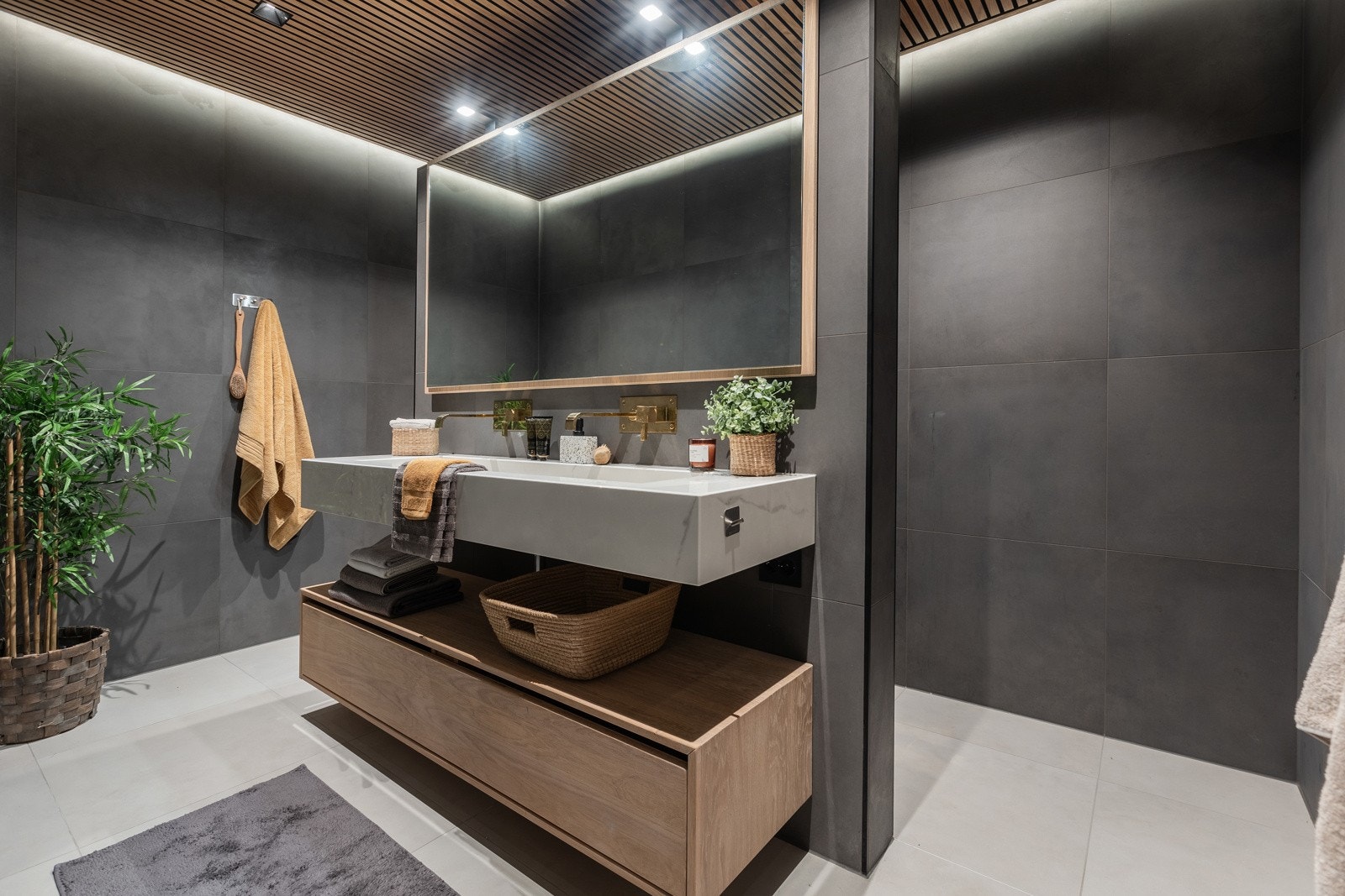 Begge badene i samme stil med flislagte mørke fliser på vegg og lyse fliser på gulv. Innfellbare dusjvegger, moderne innredning og speil med belysning. Spiltak med innfelte downlights gir badene den riktig stemningen. Vegghengt toalett. Galleribilde