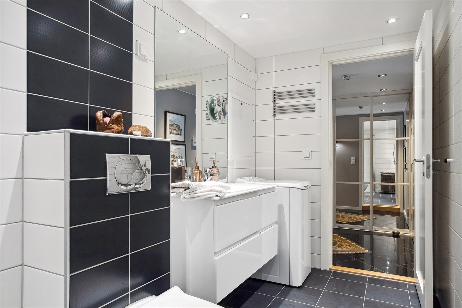 Badet er utstyrt med veggmonterte dusjvegger, veggmontert klosett og servant med skuffer og speil. Opplegg for vaskemaskin og avtrekk via mekanisk anlegg. Galleribilde