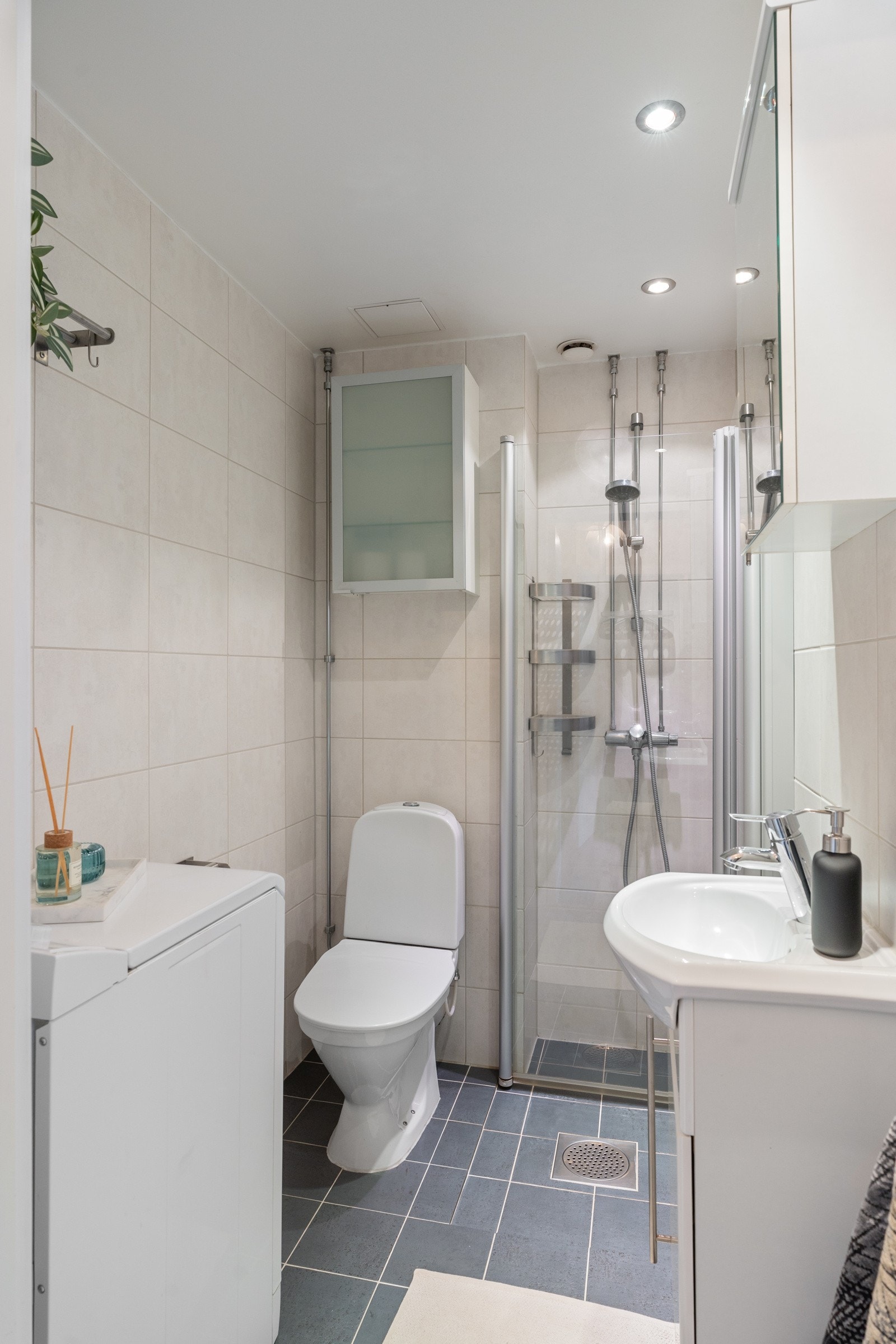 Fint, flislagt baderom som består av dushjørne, toalett, servant over innreding og speilskap på vegg. Galleribilde