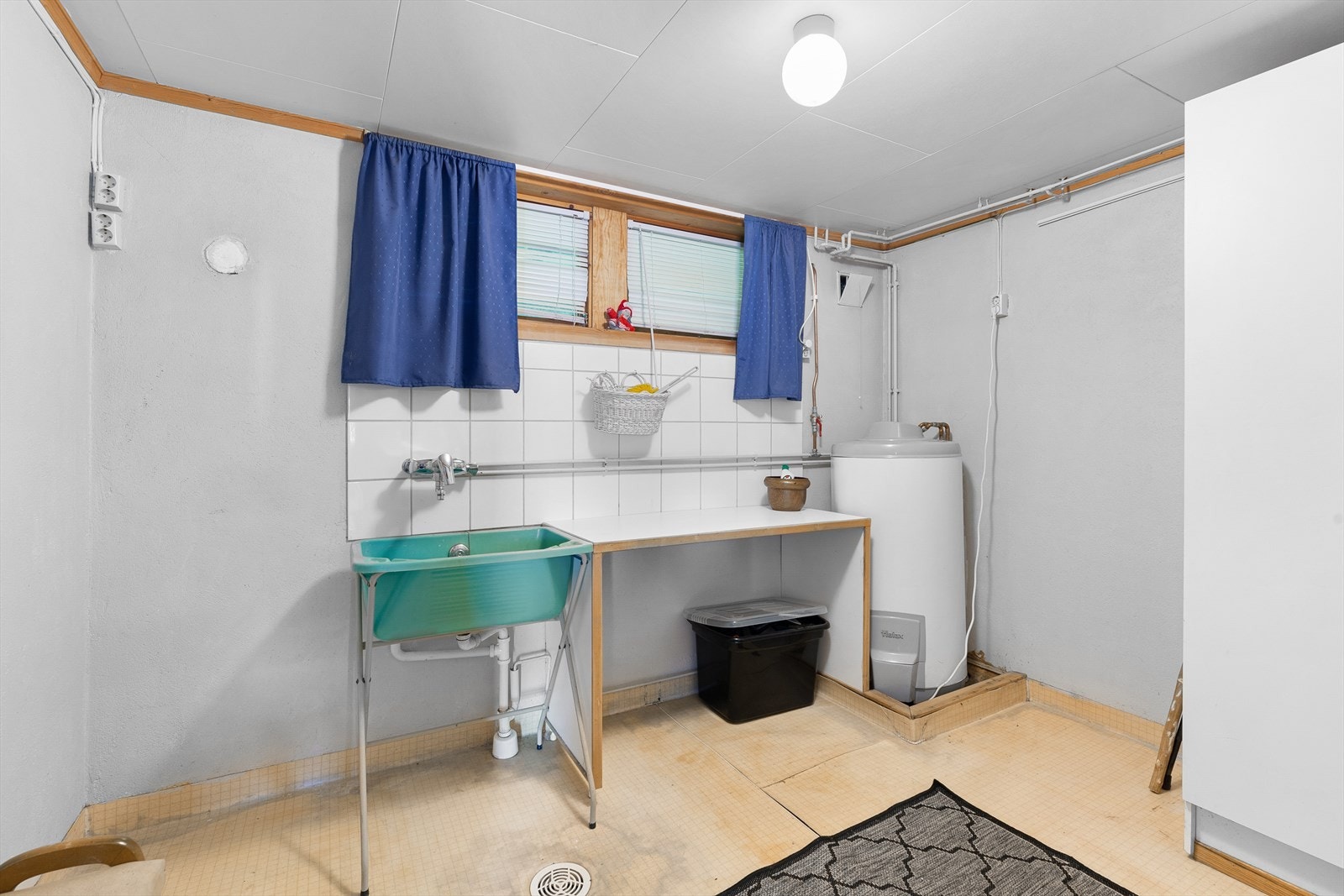 Enkelt innredet vaskerom med plast skyllekar, arbeidsbenk og røropplegg for vaskemaskin. Galleribilde