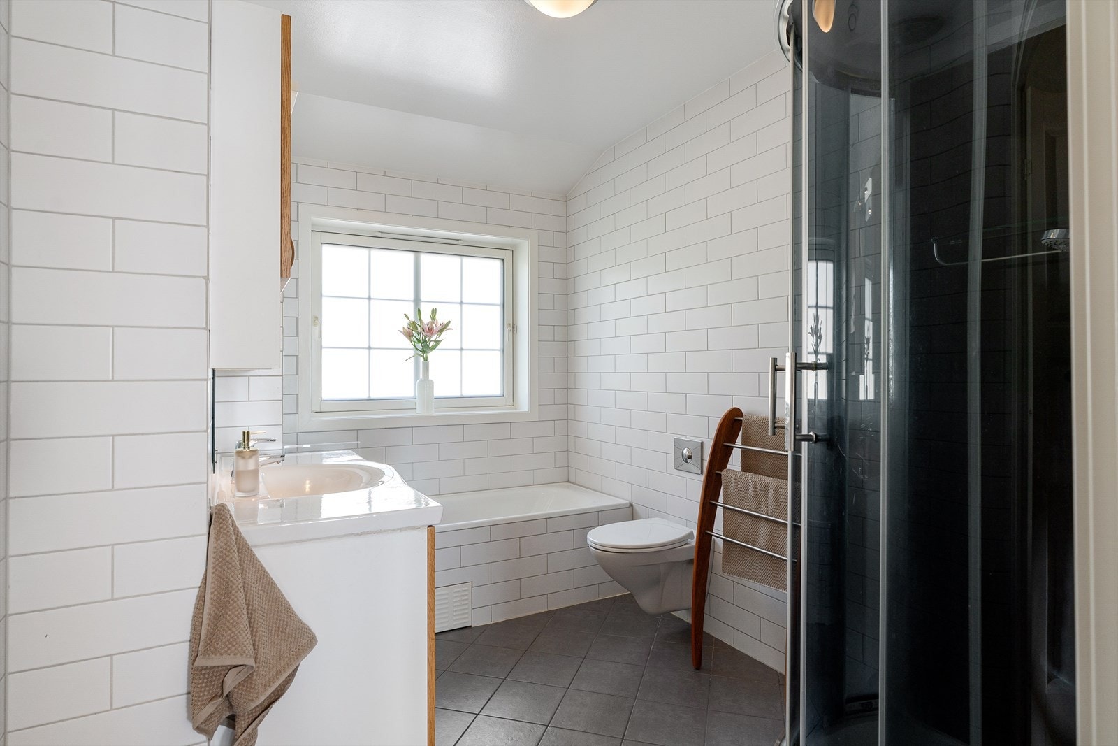 Bad har heldekkende servant, servantskap, toalettskap, speil, veggmontert wc, innbygd badekar og steamdusj. Galleribilde