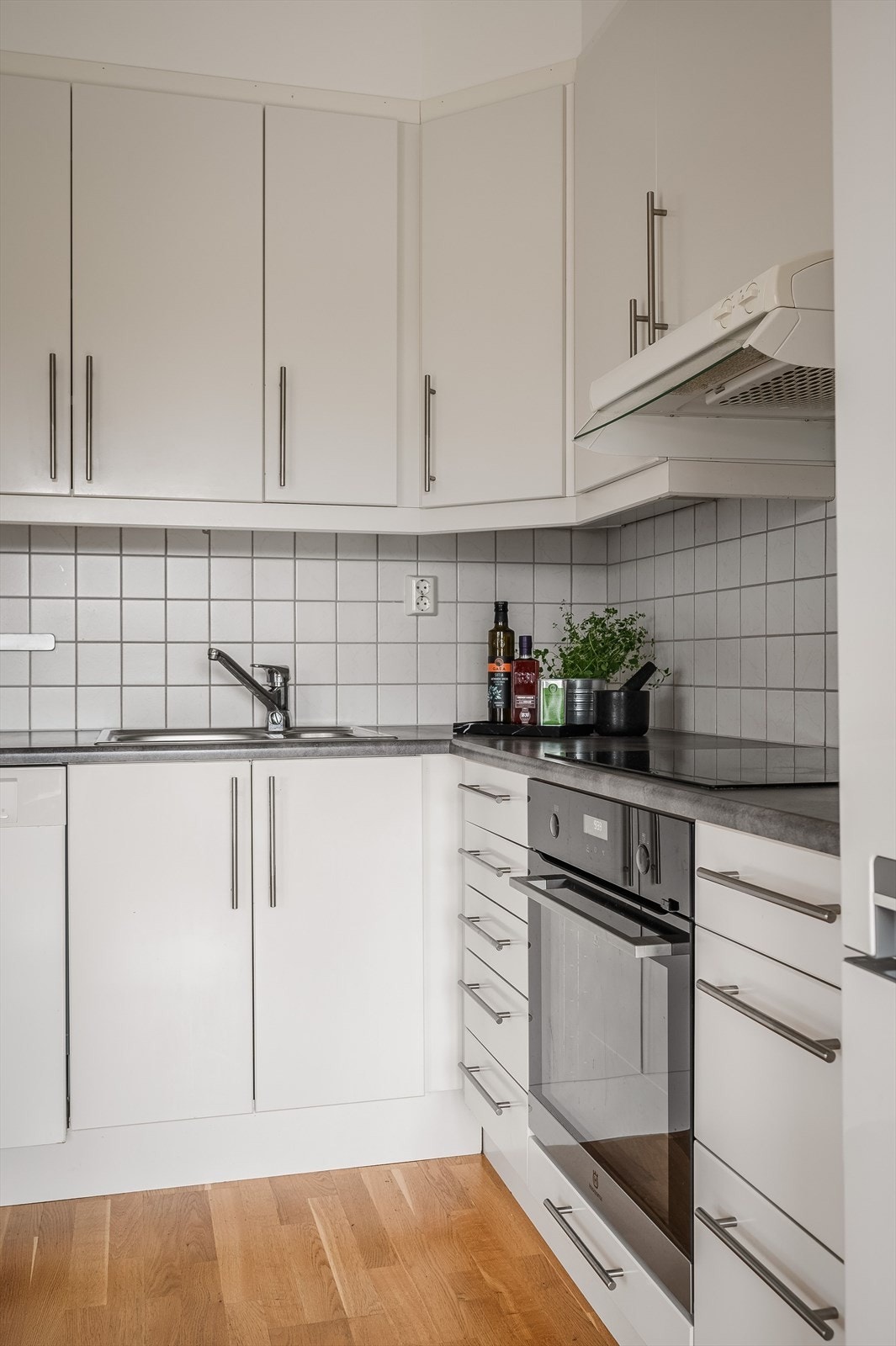 Innredningen har hvite glatte fronter og laminert benkeplate med nedfelt oppvaskkum. Praktisk med fliser i benkeryggen og belysning under overskapene. Galleribilde
