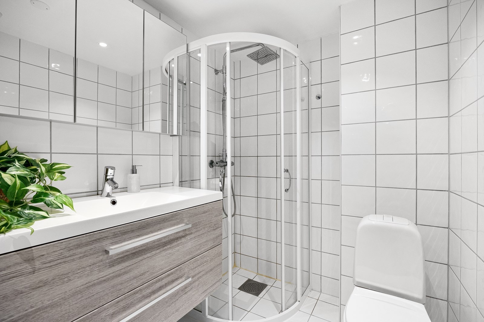 Badet er helfliset med varmekabler i gulv og er innredet med servant med underskap, speil med skap, dusjhjørne, WC og opplegg for vaskemaskin og tørketrommel. Galleribilde