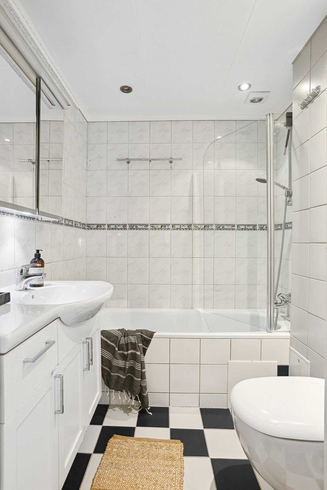 Baderommet er innredet med servantskap, speilskap, veggskap, vegghengt toalett og badekar med hengslet glassvegg på badekarskant. Galleribilde