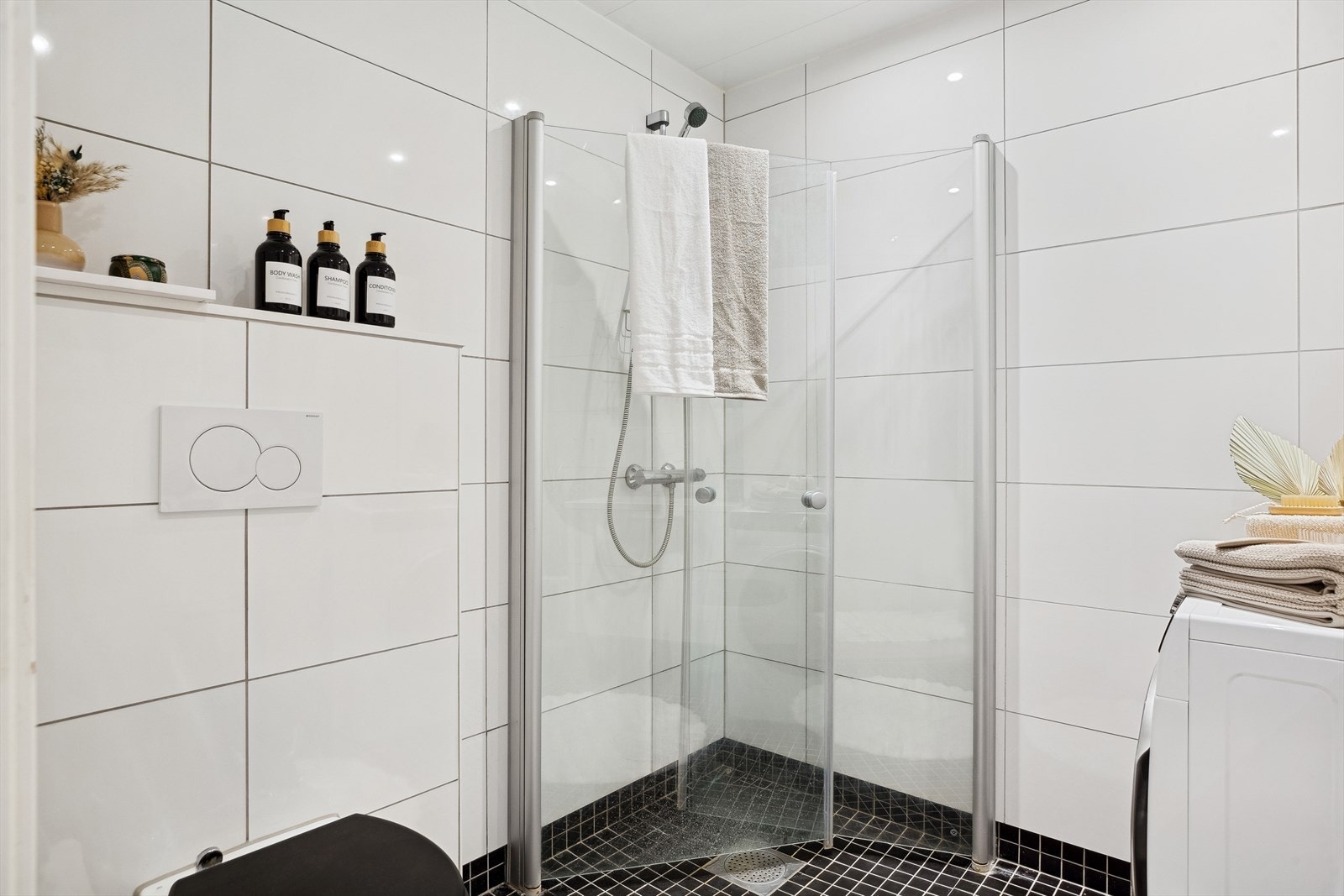 Badet har veggmontert toalett, dusjhjørne med innfellbare, rette glassdører og opplegg for vaskemaskin. Galleribilde
