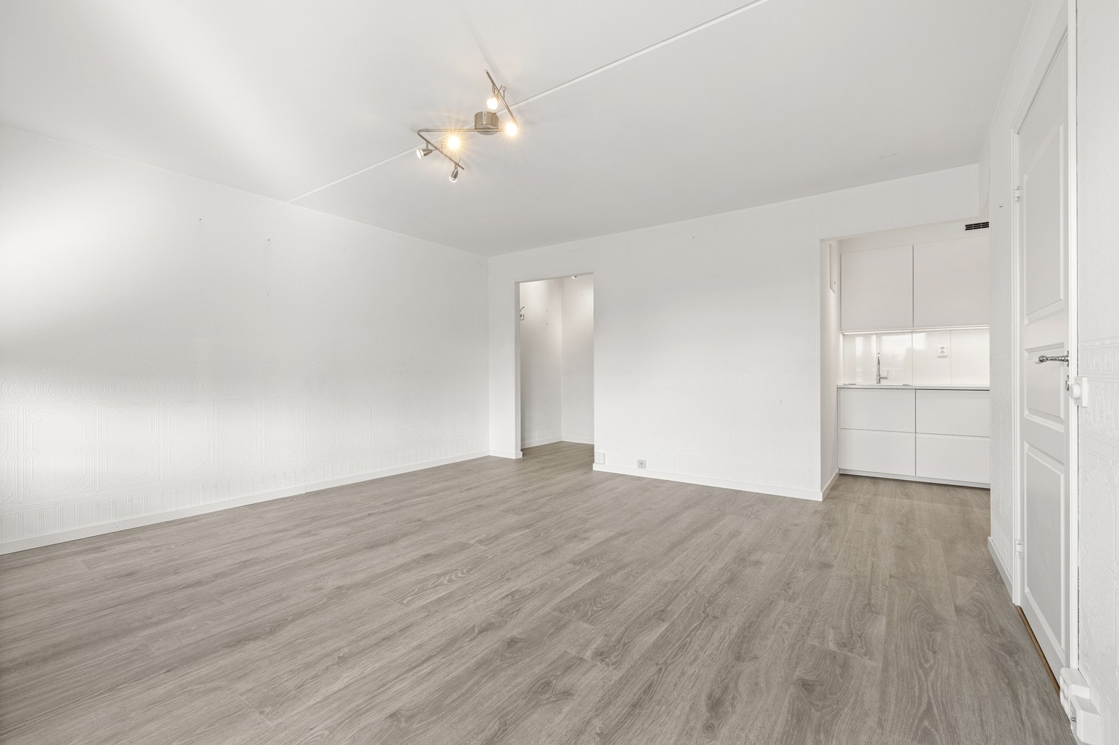 Stuen har tapetserte vegger og tak av betong i en nøytral hvit farge. Galleribilde