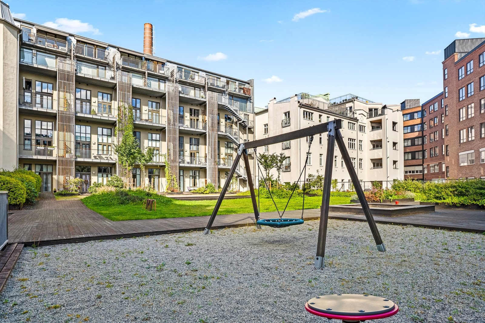 Forhøyet del av bakgården med plen, beplantning og lekeapparater. Galleribilde