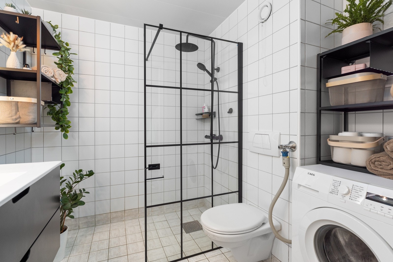 Badet er innredet med en vegghengt servant med oppbevaringsskuffer, toalett, speil med LED-belysning og et dusjhjørne med glassdør. Det er også opplegg for vaskemaskin Galleribilde