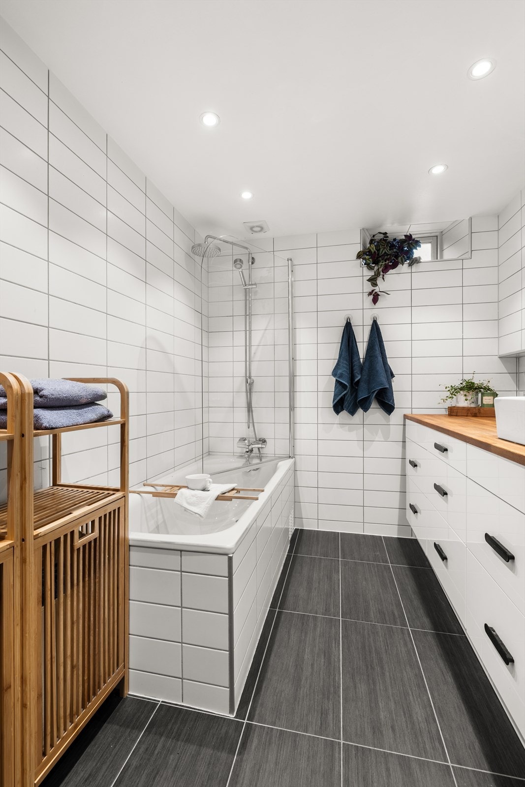 Badet er innredet med innfliset badekar med dusj, dusjvegg i glass på karet, veggmontert klosett samt to stk. servanter på benkeplate. Galleribilde