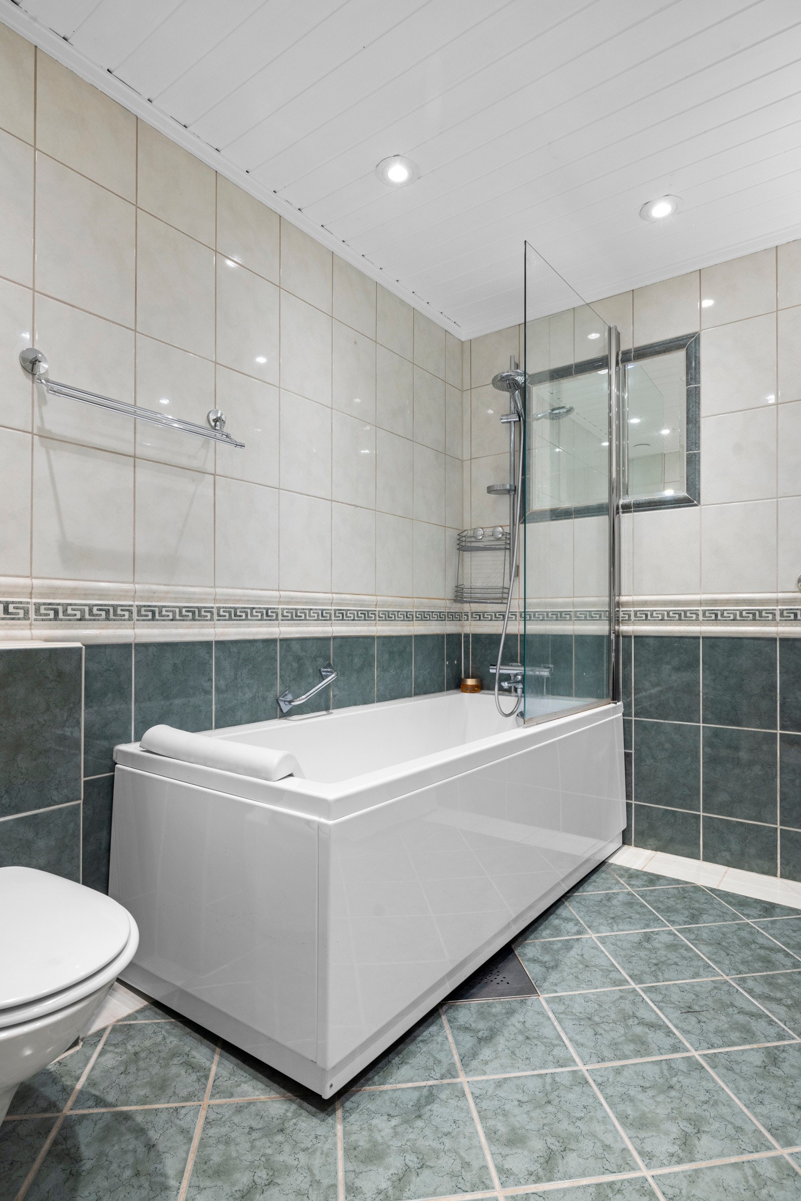 I tillegg har badet veggmontert toalett, samt et badekar med svingbar dusjdør i glass Galleribilde