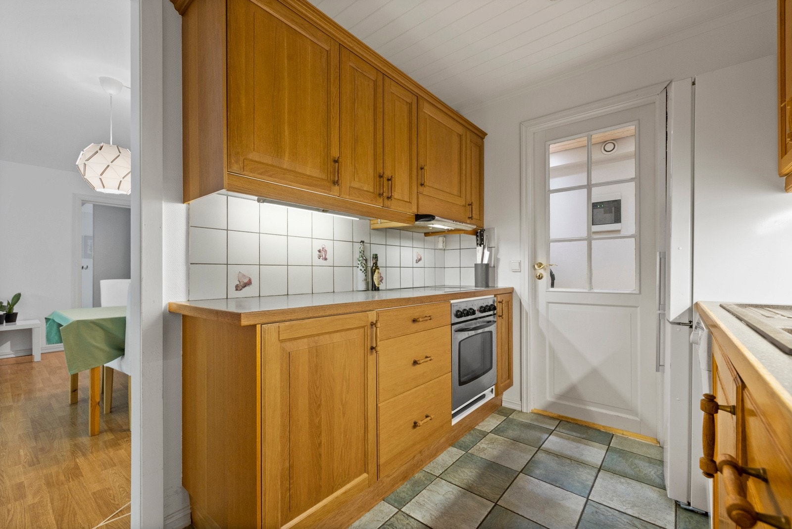 Kjøkkeninnredningen har vitrineskap, profilerte trefronter og laminert benkeplate med benkebeslag og oppvaskkum Galleribilde